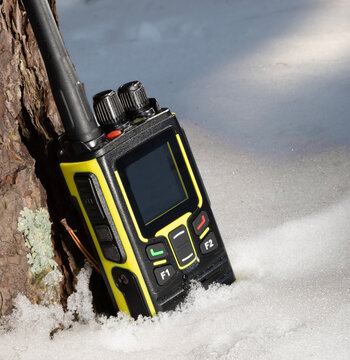Black and yellow walkie talkie resting against a tree in the snow