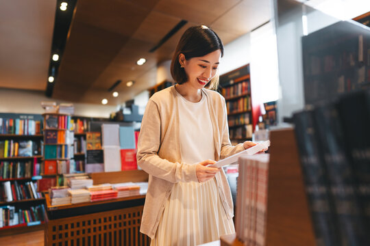 Portrait of young adult southeast asian woman reading book at bookstore shop