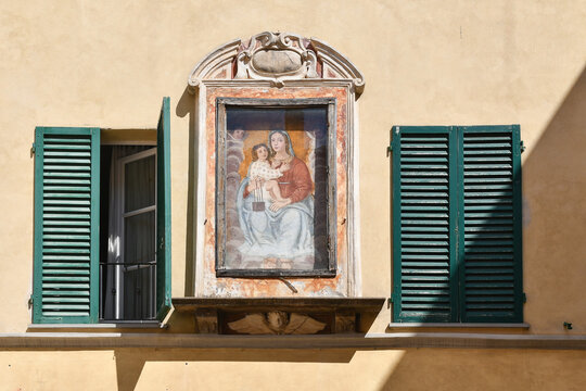 Traditional street tabernacle with a fresco of the Madonna and Child between green window shutters, Lucca, Tuscany, Italy