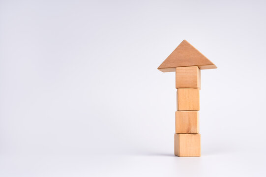 Wooden blocks form an upward arrow on minimal white background with copy space. Business growth, progress, performance improvement, career advancement, strategy and goal achievement concept.