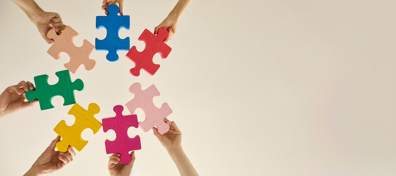 Hands hold colorful puzzle pieces for teamwork. People arrange bright jigsaw shapes with copy space for business unity, community projects, and problem solving. Unity creates shared solutions.