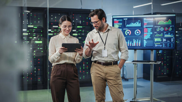 Technical specialists discussing data on a tablet in server room.