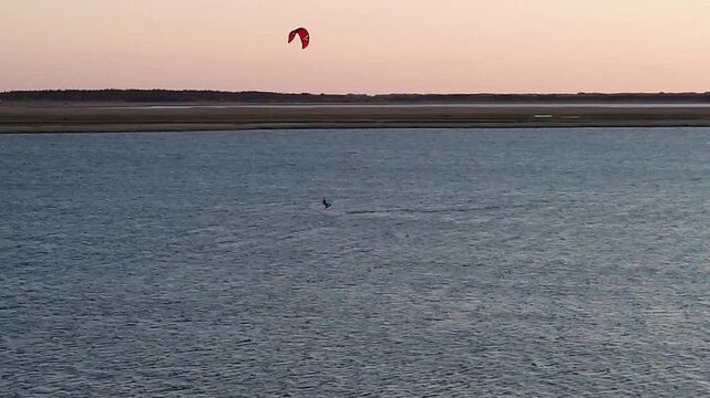 Drone aerial shot of a kitesurfer performing a high jump over the water and crashing during a colorful sunset in Bork Havn