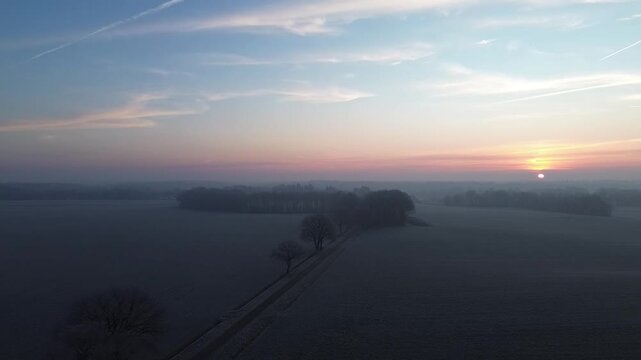 Slow drone flight over farmland fields during a vibrant sunset with the sun hanging just above the horizon in Drenthe