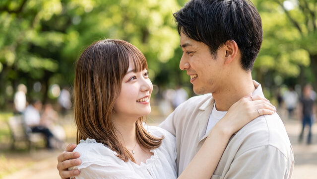 Young Japanese couple smiling and hugging outdoors in a green park during daytime.