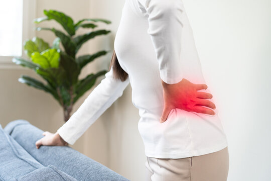 Asian young woman suffering from severe lower back pain and lumbar muscle injury while standing at home, backache and office syndrome concept for medical and health care person.