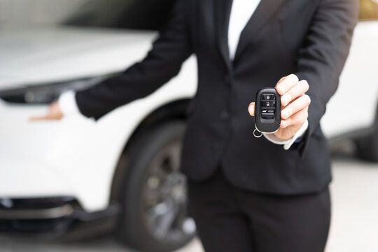 Close up of business woman holding smart car keyless remote control, presenting new automobile to buyer or client for rental service or dealership in showroom, transport and insurance concept.
