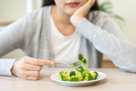 Diet in bored concept, Ketogenic, Low carb, Intermittent Fasting young woman dieting holding fork at broccoli on salad plate tired with eat fresh vegetables. Nutrition clean, healthy food good taste.