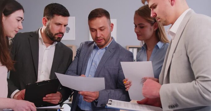 Busy motivated office company employees discuss together business project documents paper at briefing, diverse colleagues brainstorm at meeting sharing considering ideas for collaboration, teamwork