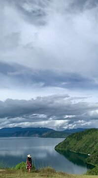 Rear view of a female tourist walking slowly toward breathtaking Lake Toba panorama at Tara Bunga Hills, North Sumatera, Indonesia. Calm, inspiring outdoor footage for travel and lifestyle.