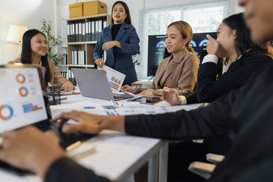Business team analyzing data during office meeting. Asian business professionals collaborating in office, analyzing financial data and charts.