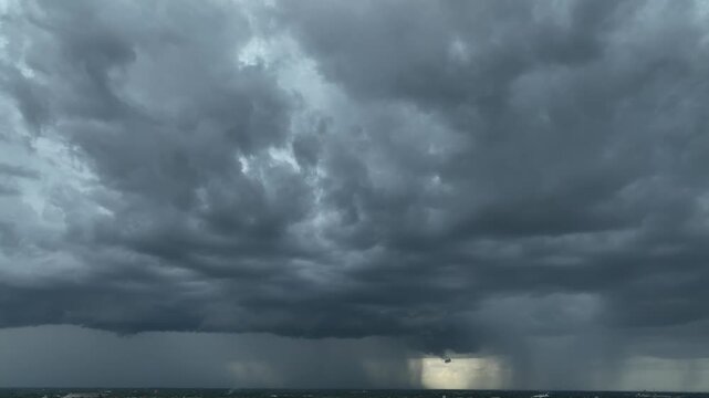 Aerial panorama shows dense storm clouds and heavy rain sweeping across the horizon, conveying extreme weather, changing climate patterns and increasing atmospheric instability.

