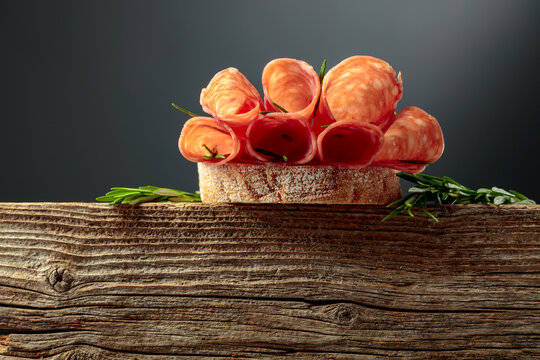 Sandwich with thin slices salami and rosemary on a wooden table.