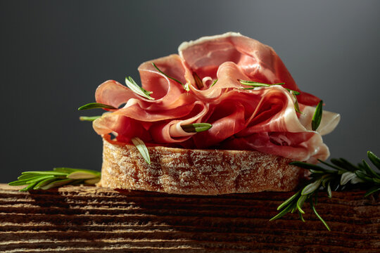 Sandwich with thin slices of Italian dry cured prosciutto, served on an old, weathered board.