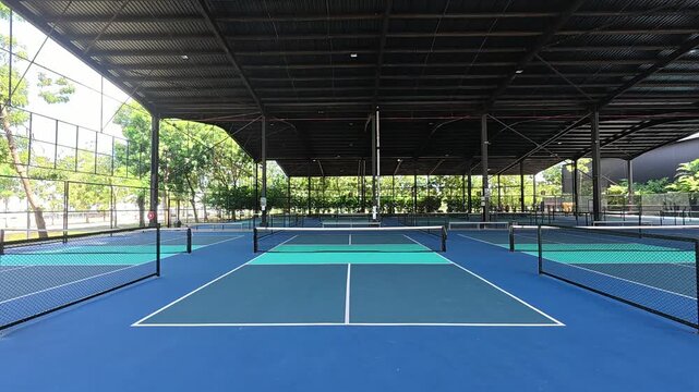 An empty covered pickleball court sits ready for play. The modern facility features a well-maintained surface, clean markings, and protective surrounding mesh nets.