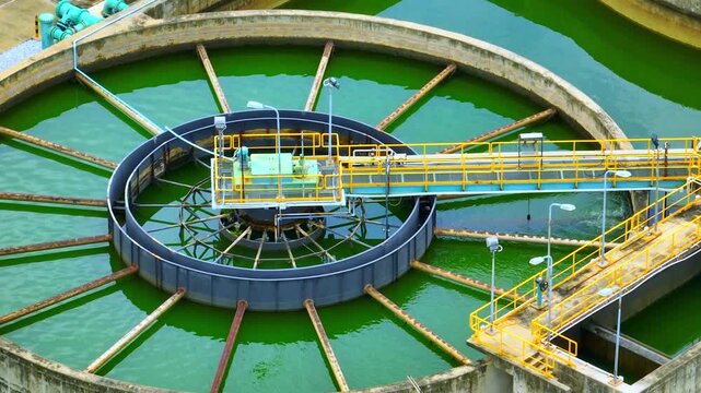Aerial perspective of an industrial water treatment clarifier shows green wastewater, radial structures and mechanical systems, reflecting modern sanitation technology and environmental protection.

