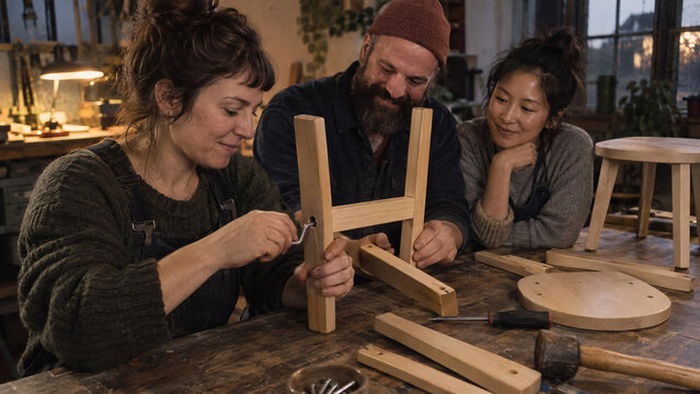 Diverse group of adult students learning carpentry assembling wooden furniture in craft workshop. Concept of education, instructions, learners, assemble, woodworking class, craft lesson.