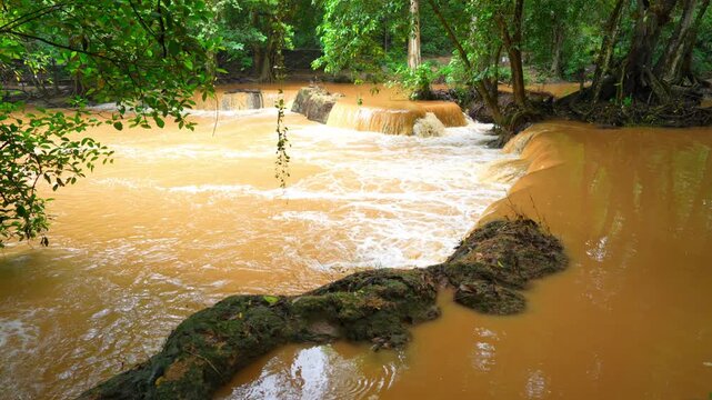 Severe runoff transforms this tropical waterfall into a powerful muddy torrent, symbolizing flash floods, land degradation, and the real impact of global warming on modern landscapes. Thailand.
