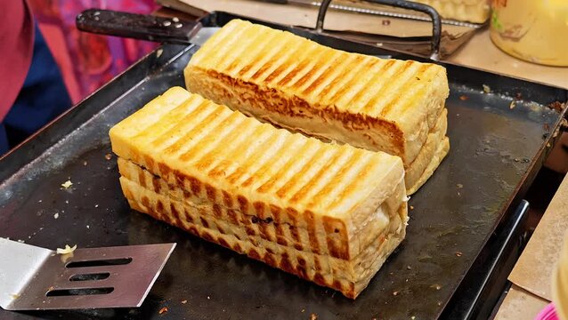 Chef hands holding spatula cooking sweet toast bread on flat iron griddle pan, traditional Indonesian street food cuisine concept. 4K