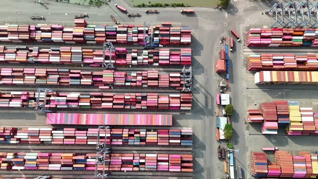 Top-down drone view of a crane stacking colorful cargo containers at a port terminal.