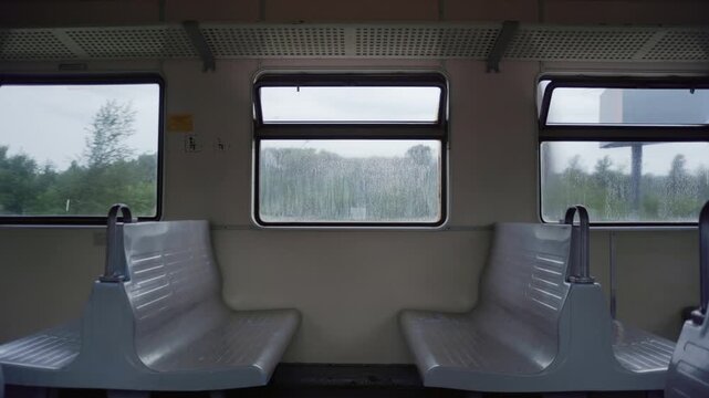Wide shot from inside a moving train showing empty seats and three windows as the countryside passes by. Ideal for travel, journey, and transportation themes.