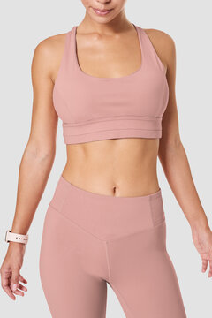 Fit woman in pink sports bra and leggings posing on gray background