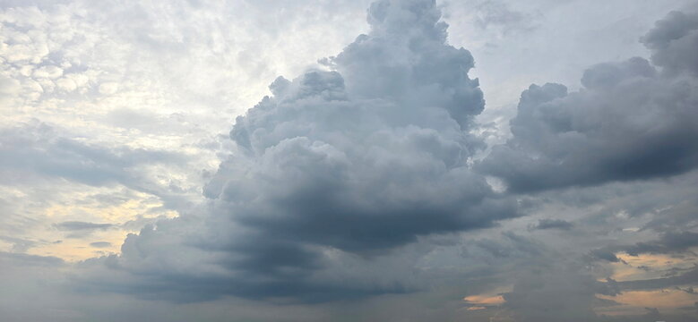 Large, dense cloud formation may be developing into a thunderstorm. Cumulus and Cumulonimbus clouds are present against a gray sky tinged with patches of orange. These are thick, vertical development.