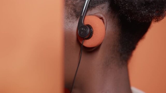 Anonymous black woman putting on vintage headphones against orange studio background with copyspace.