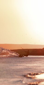 Kite surfer carving through the waves and jumping with a kite against a glowing sunset