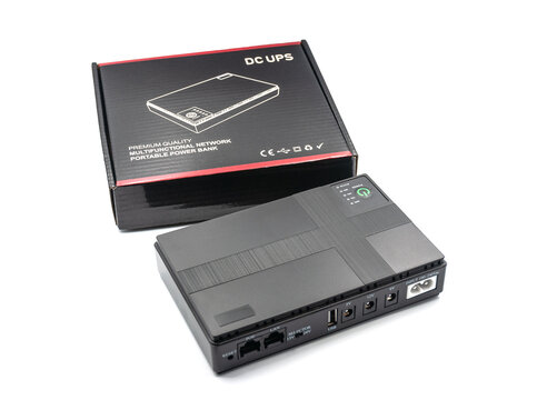 Portable DC UPS power bank for network routers and modems, shown next to its original packaging, isolated on a white background.