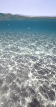 Crystal blue sea underwater and sandy sea bottom on a sunny day, vertical screen