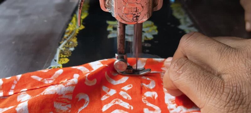 Close up view of sewing machine needle stitching vibrant orange and white patterned fabric cloth