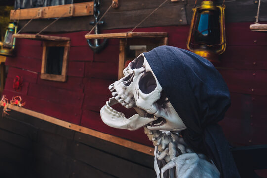 Halloween pirate ship decoration background with skeleton pirate with bandana, carved jack o lantern pumpkins, gravestones, and Happy Halloween sign outdoor. Spooky Halloween party outdoor decoration.