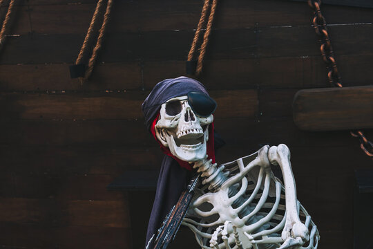 Decorative pirate skeleton prop with bandana and eye patch on wooden ship background. Human skeleton prop, creatively dressed as pirate on deck to be replica pirate ship. Perfect for Halloween concept