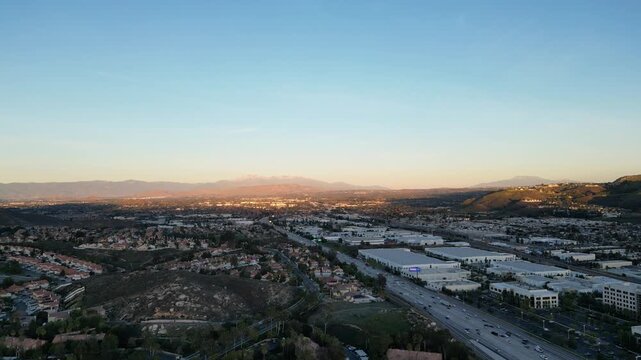 Aerial over commercial buildings, residential neighborhoods, hillsides and Riverside 91 Freeway in Corona, California during sunset. Riverside County, Inland Empire near Los Angeles. January, 2024.