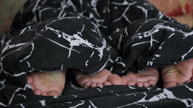 The legs of a woman and a man side by side in bed. A couple sleeping under a black blanket. A romantic moment. Relationships and intimacy between lovers. Bare feet under the blanket.