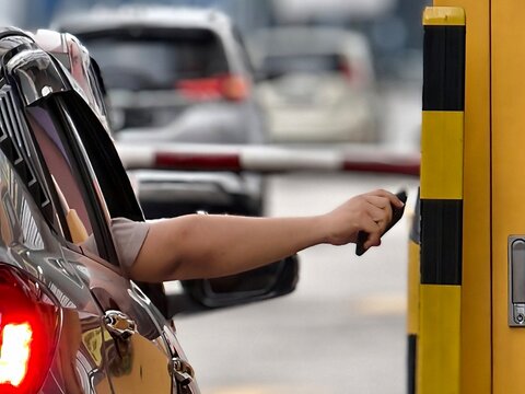 Driver using smart card payment at a parking gate barrier for seamless and cashless transaction.