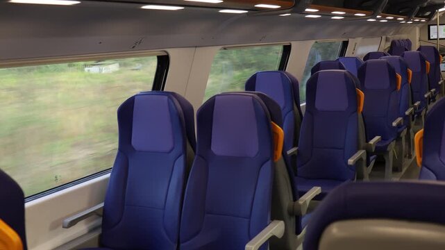 Empty blue passenger seats with yellow handles inside modern train carriage, showing travel