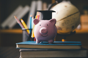 Piggy bank wearing a graduation cap on stacked books with a globe and pencils, representing education savings, tuition planning, scholarship, student finance, college costs, and future investment. © Manasanan Wongchoomp