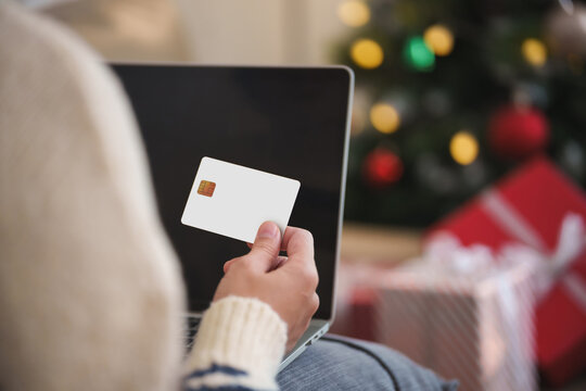 Woman holding a credit card while shopping online on a laptop at Christmas, representing holiday payment, e-commerce, seasonal spending, cashless checkout, festive discounts and retail sales.