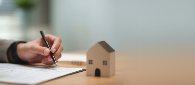 Female loan officer points to a mortgage document and reviewing a property contract, showing a customer where to sign during a home loan process.