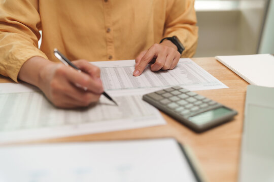 Female reviewing financial documents with a pen and calculator at a desk, representing accounting, bookkeeping, budgeting, expense analysis, tax review and business finance planning.
