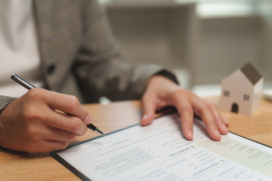 Mortgage officer reviewing and signing a home loan document beside a model house, representing real estate financing, property purchase, lending, contract approval and mortgage processing.