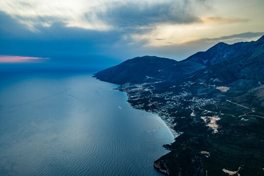 Oblique aerial view of a mountainous coastal town and bay near Plazhi i Jal&euml;s at dusk