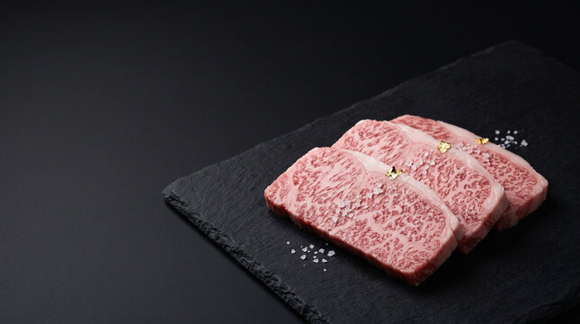 Raw premium marbled wagyu beef steaks garnished with edible gold leaf on black slate with copy space
