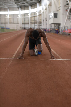 Unrecognizable black runner preparing to sprint on track