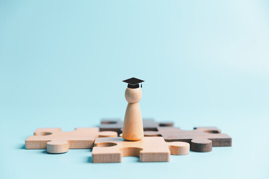 Education and career development concept with graduate wooden person standing on puzzle pieces, symbolizing learning, skills, qualification, opportunity, achievement and successful future.