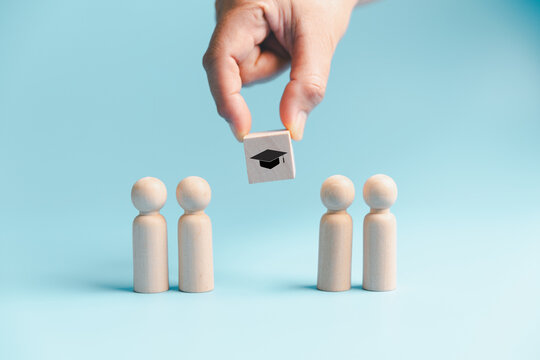 Education selection concept with hand choosing graduation symbol above wooden people, representing student admission, scholarship, academic opportunity, recruitment and future learning.