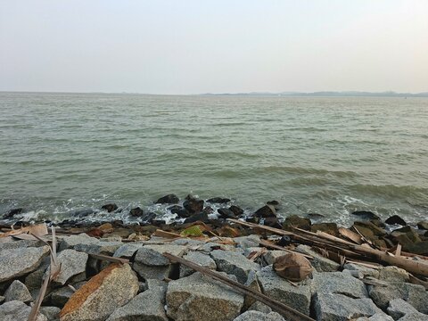 "View of the rocky coastline embankment at Karimun island, Riau Islands, Indonesia, with calm sea waves during an overcast day."