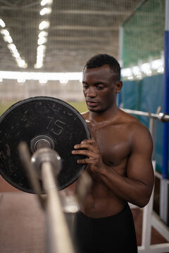 Black sportsman putting weight on bar
